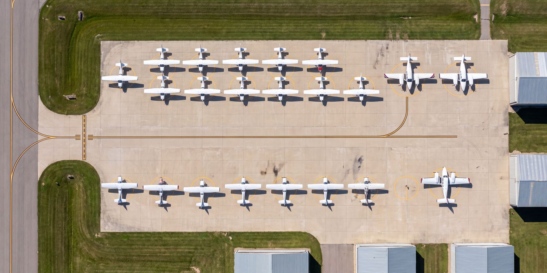 Overhead aerial view of general-aviation aircraft parked in rows on a small airport apron with painted tie-down markings