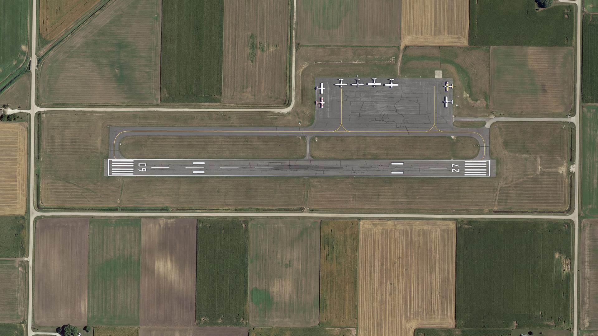 Overhead aerial view of a small regional airport runway, taxiway and apron surrounded by farmland parcels