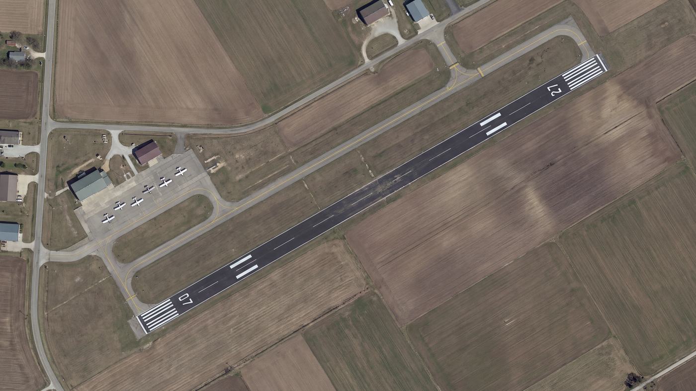 Overhead aerial view of a small airport runway and apron within surrounding parcel boundaries